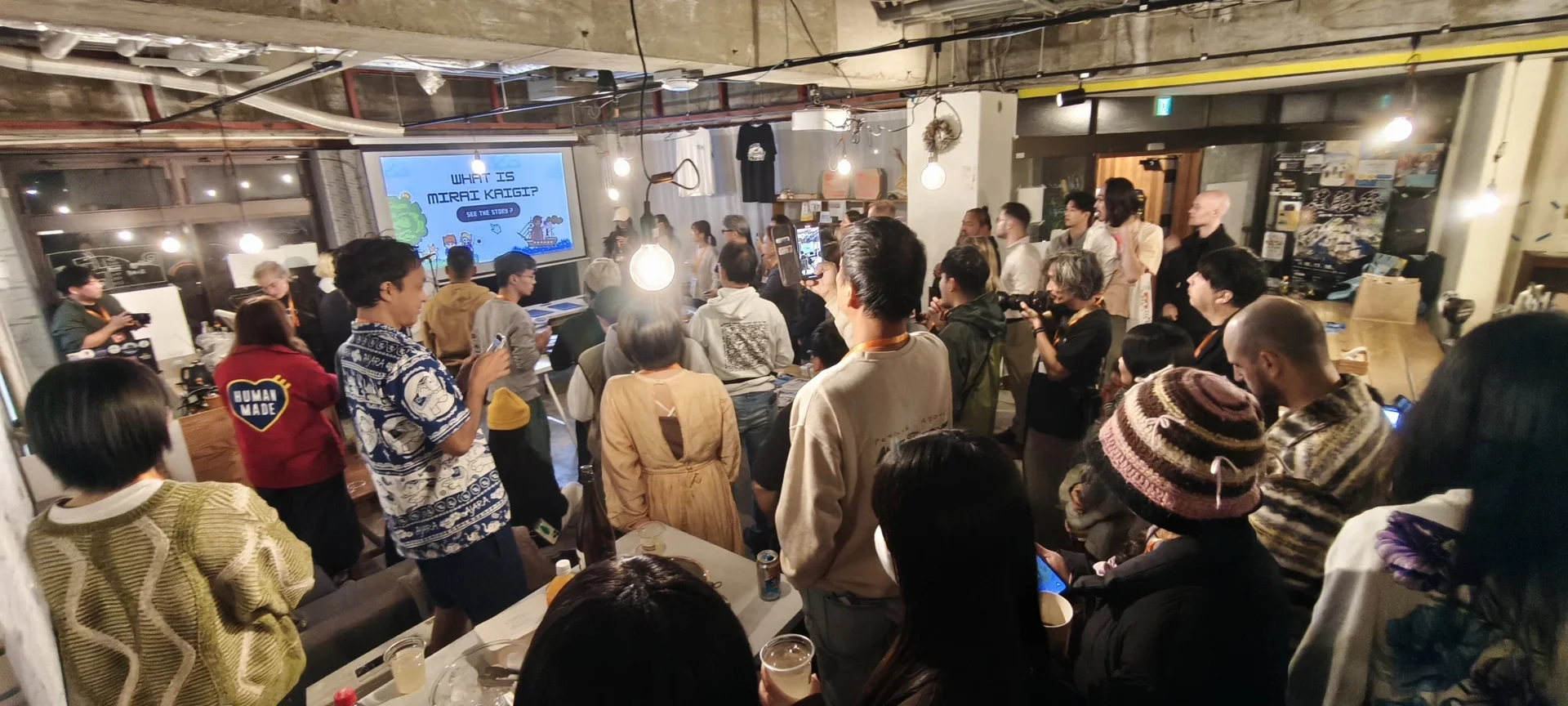 スクリーンを囲み、たくさんの人が集うイベントのひとこま。