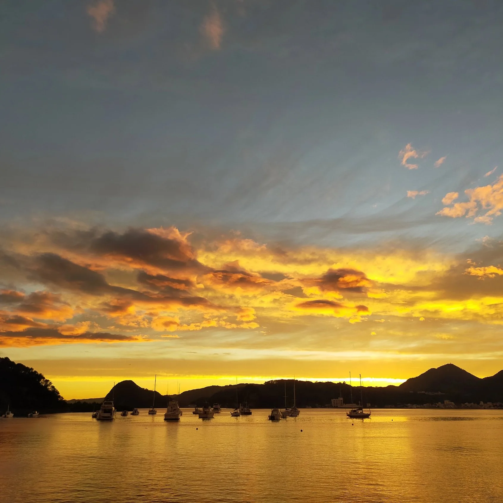 下田湾の夕焼け。黄金色の水面に、ヨットが浮かぶ。